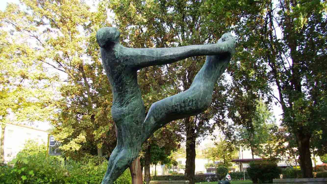Scultura in bronzo verde di due figure che danzano in un parco alberato