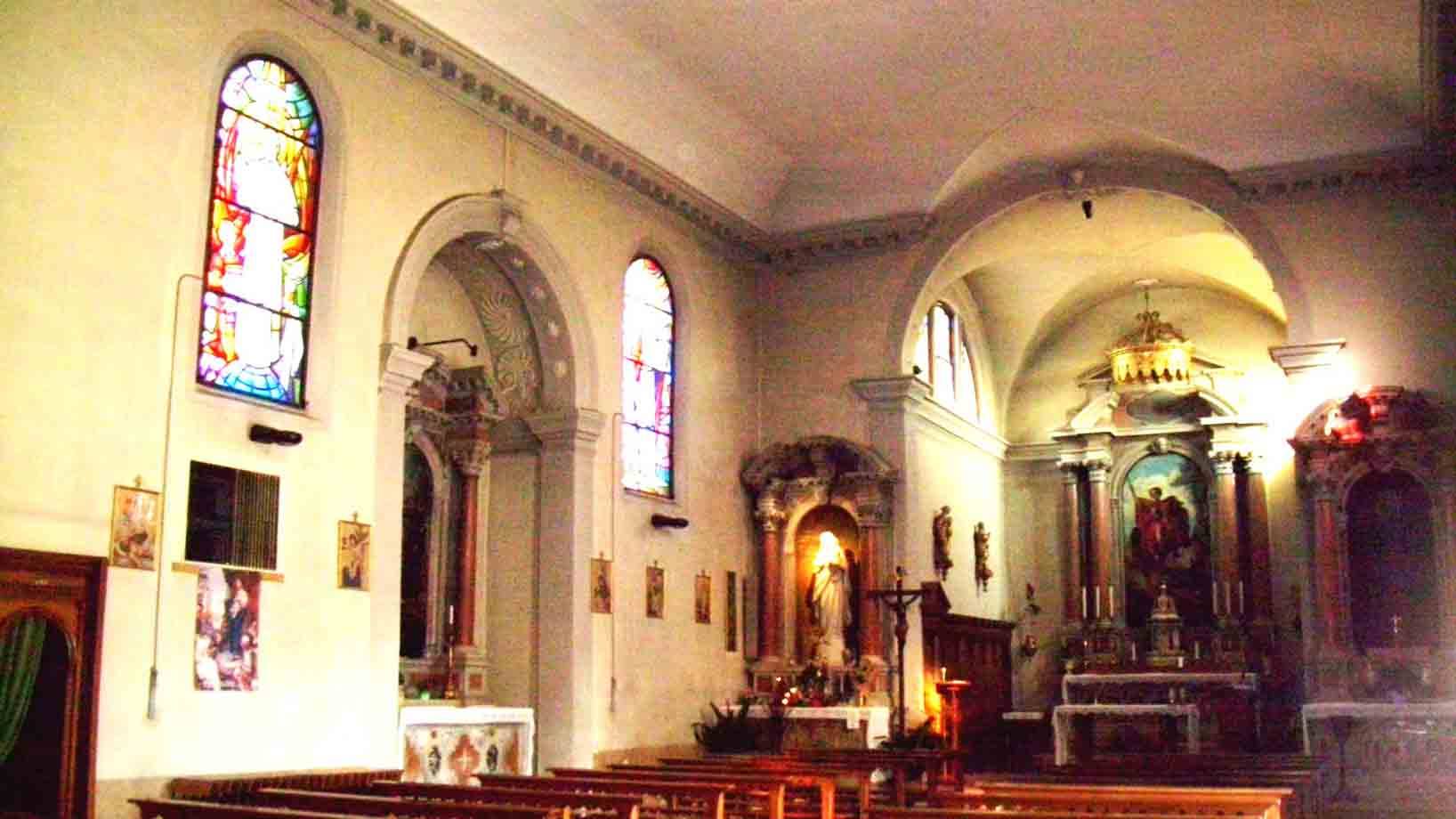 Interno di chiesa con vetrate colorate, altare decorato e banchi in legno