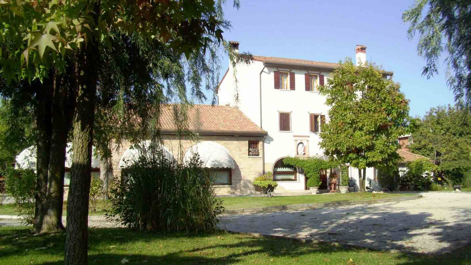 Casa colonica bianca con tetti in coppi tra alberi e giardino verde