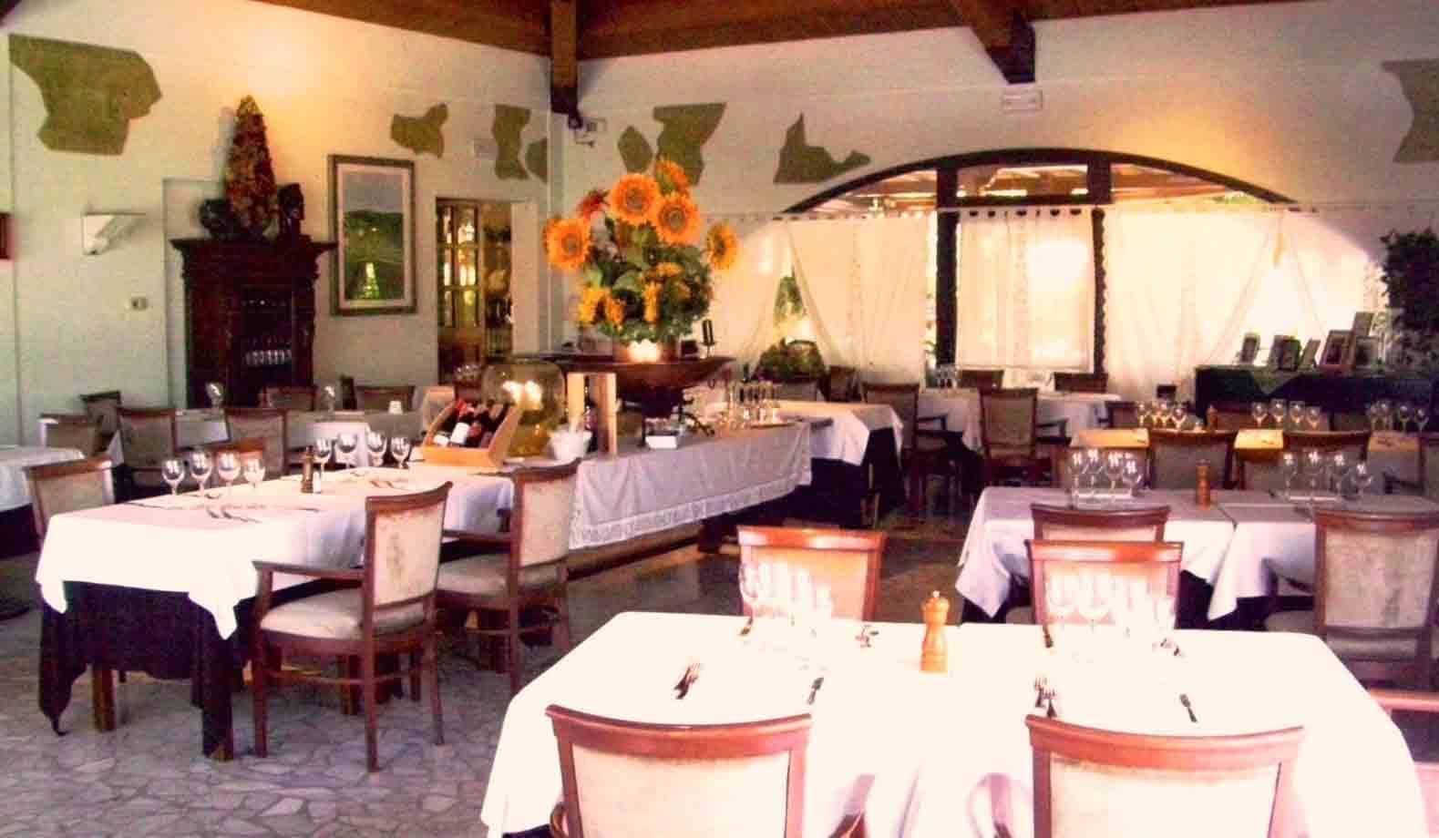 Sala ristorante con tavoli apparecchiati a tovaglia bianca e mazzo di girasoli