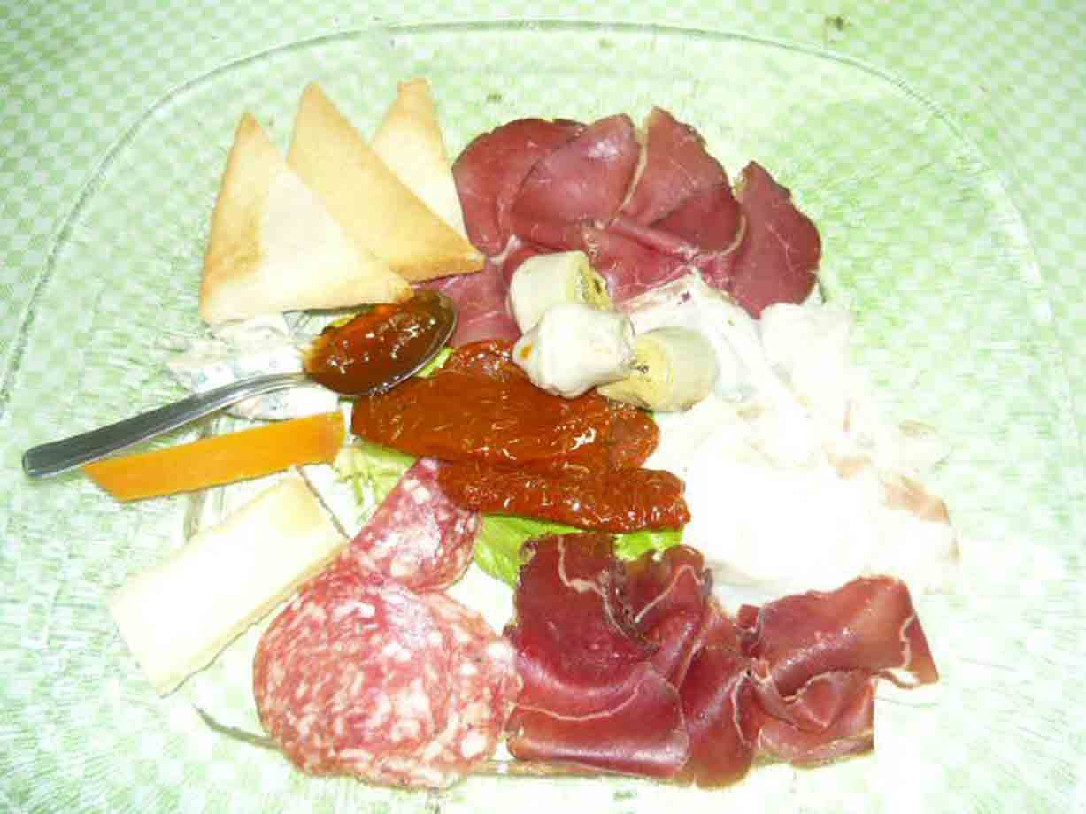Piatto di vetro con salame, prosciutto, formaggi, peperoni e pane tostato