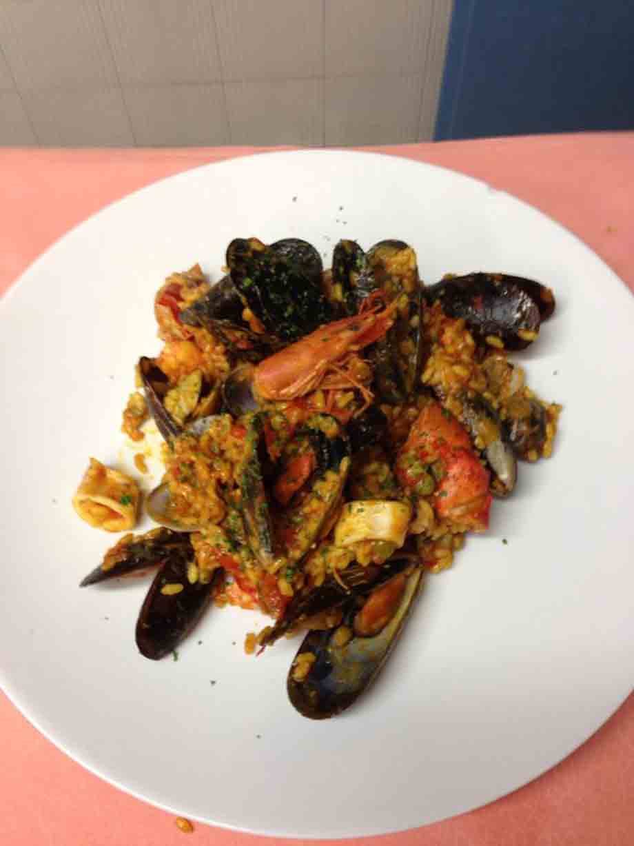 Piatto bianco con riso alla marinara: cozze, gamberi e calamari su tovaglia rosa