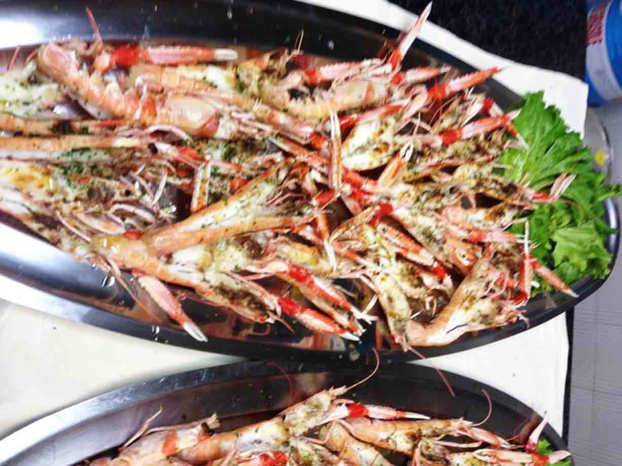 Vassoi di metallo pieni di scampi alle erbe con foglie di sedano