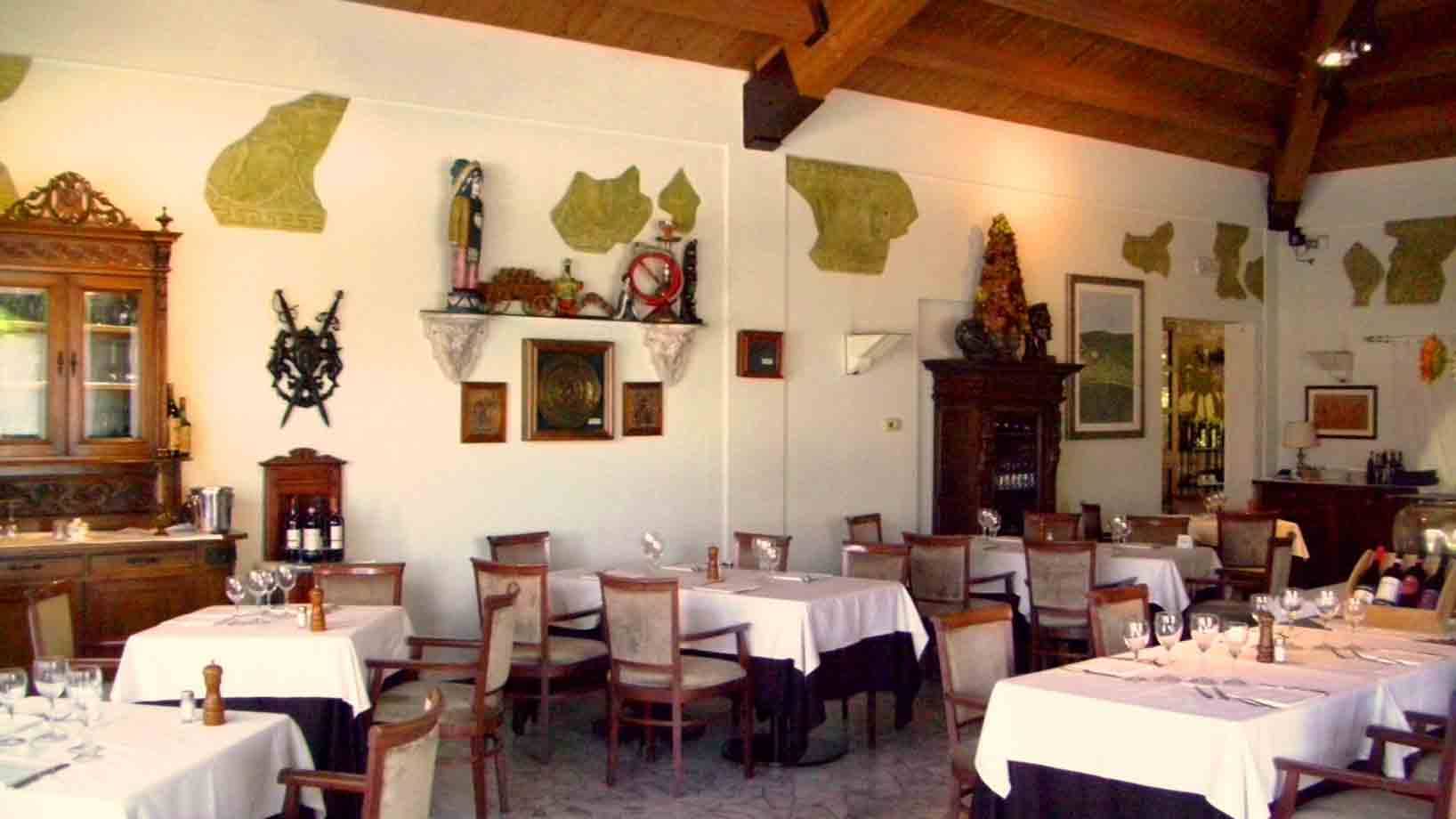 Sala di ristorante con tavoli apparecchiati a tovaglia bianca, mobili antichi e travi in legno