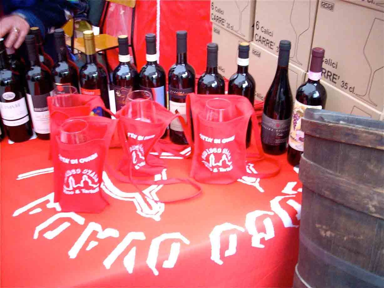 Bottiglie di vino su tovaglia rossa, borsine rosse e botte di legno