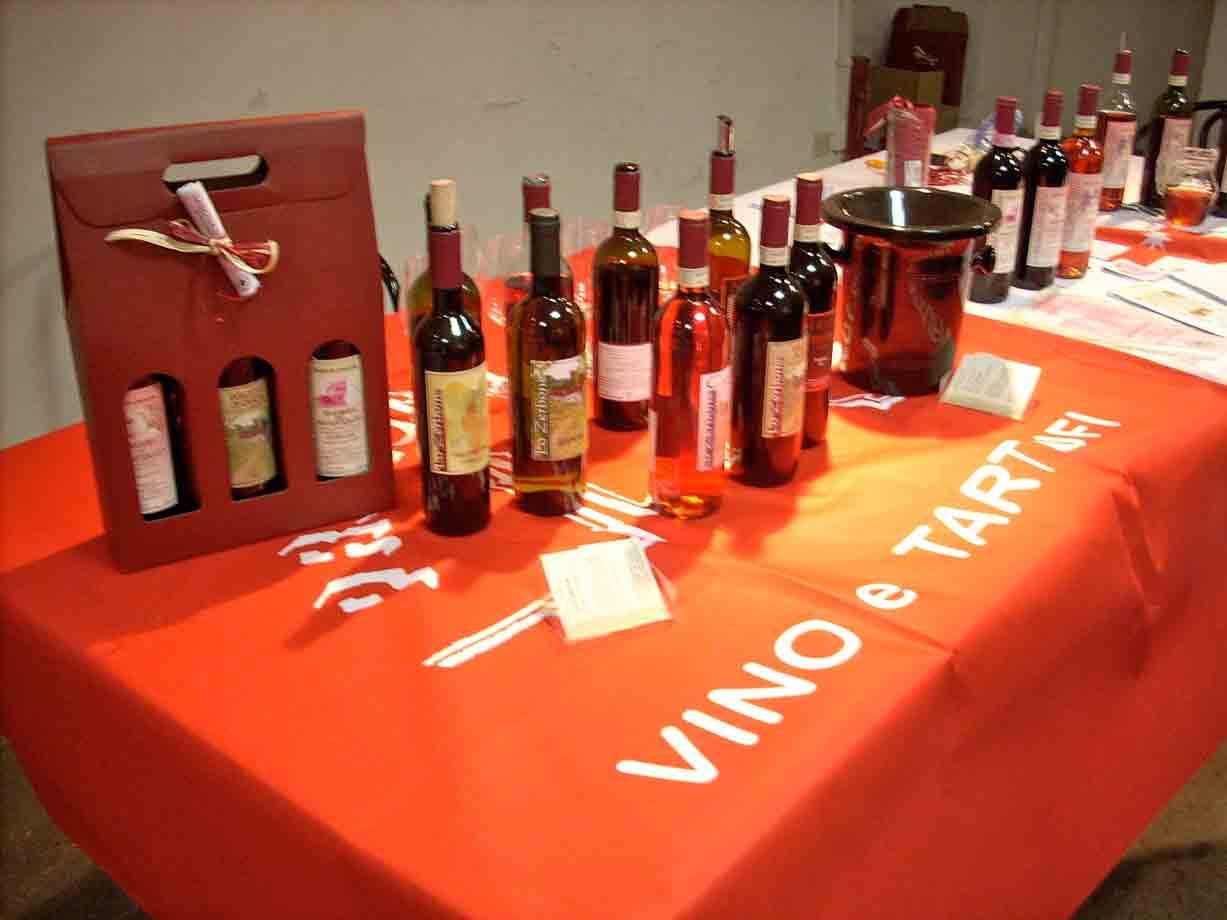 Bottiglie di vino in mostra su tavolo con tovaglia arancione scritta VINO e TARTUFI