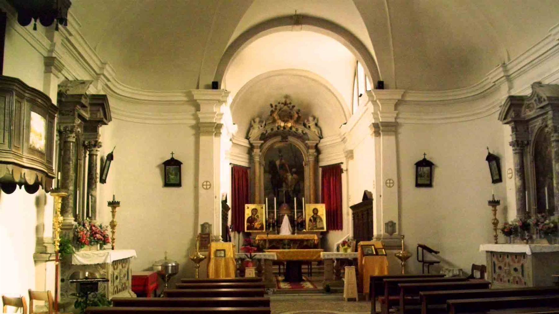 Interno di chiesa barocca con altare maggiore, candele e panche in legno