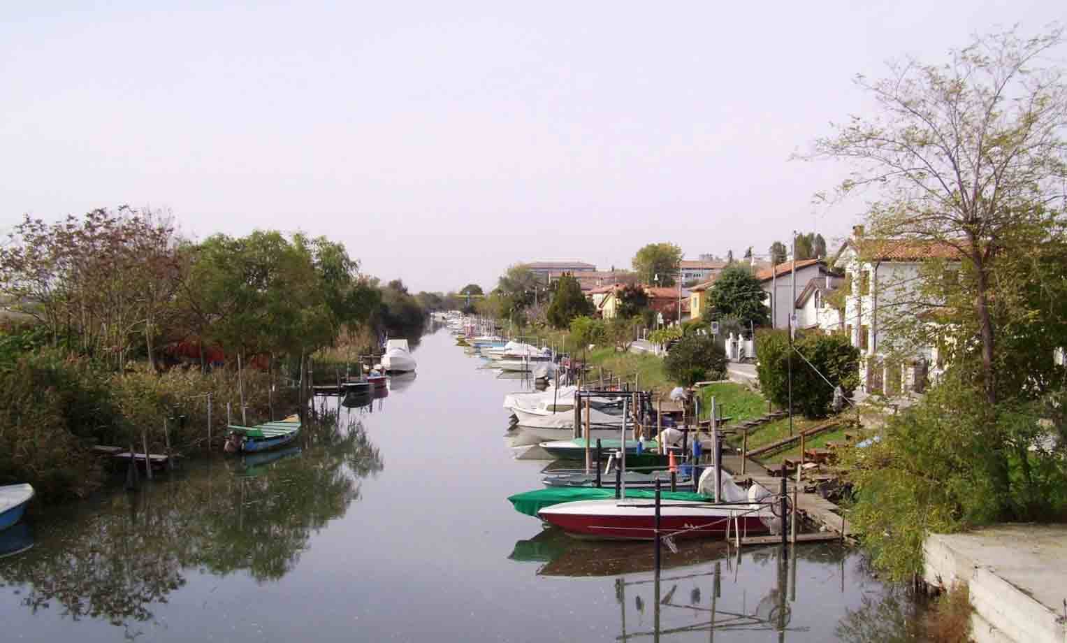Barche ormeggiate lungo un canale con case e alberi sui lati