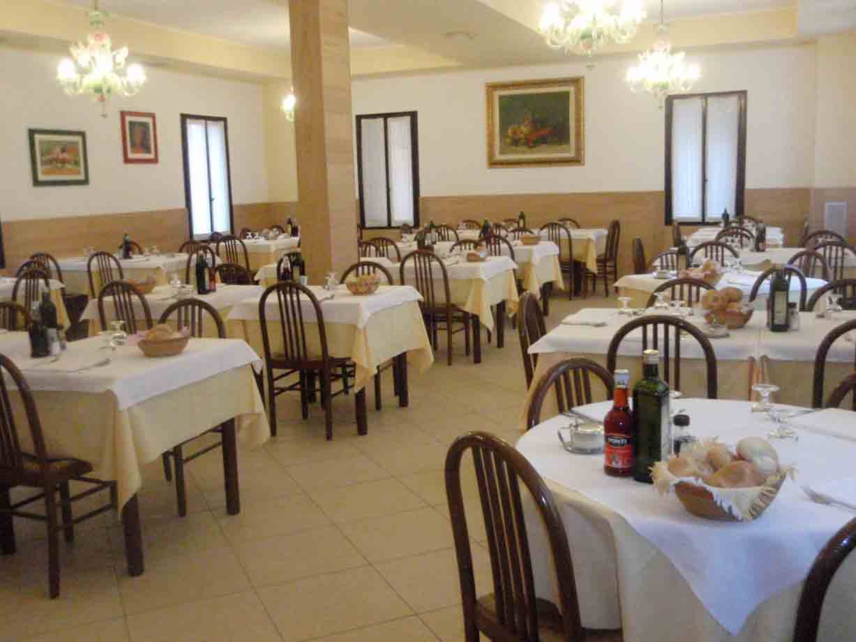 Sala da pranzo con tavoli apparecchiati a tovaglia bianca, pane e vino, lampadari accesi