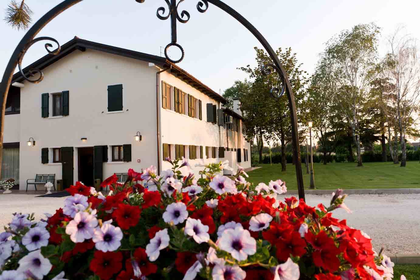 Petunie rosse e bianche in primo piano davanti a casa bianca con persiane verdi