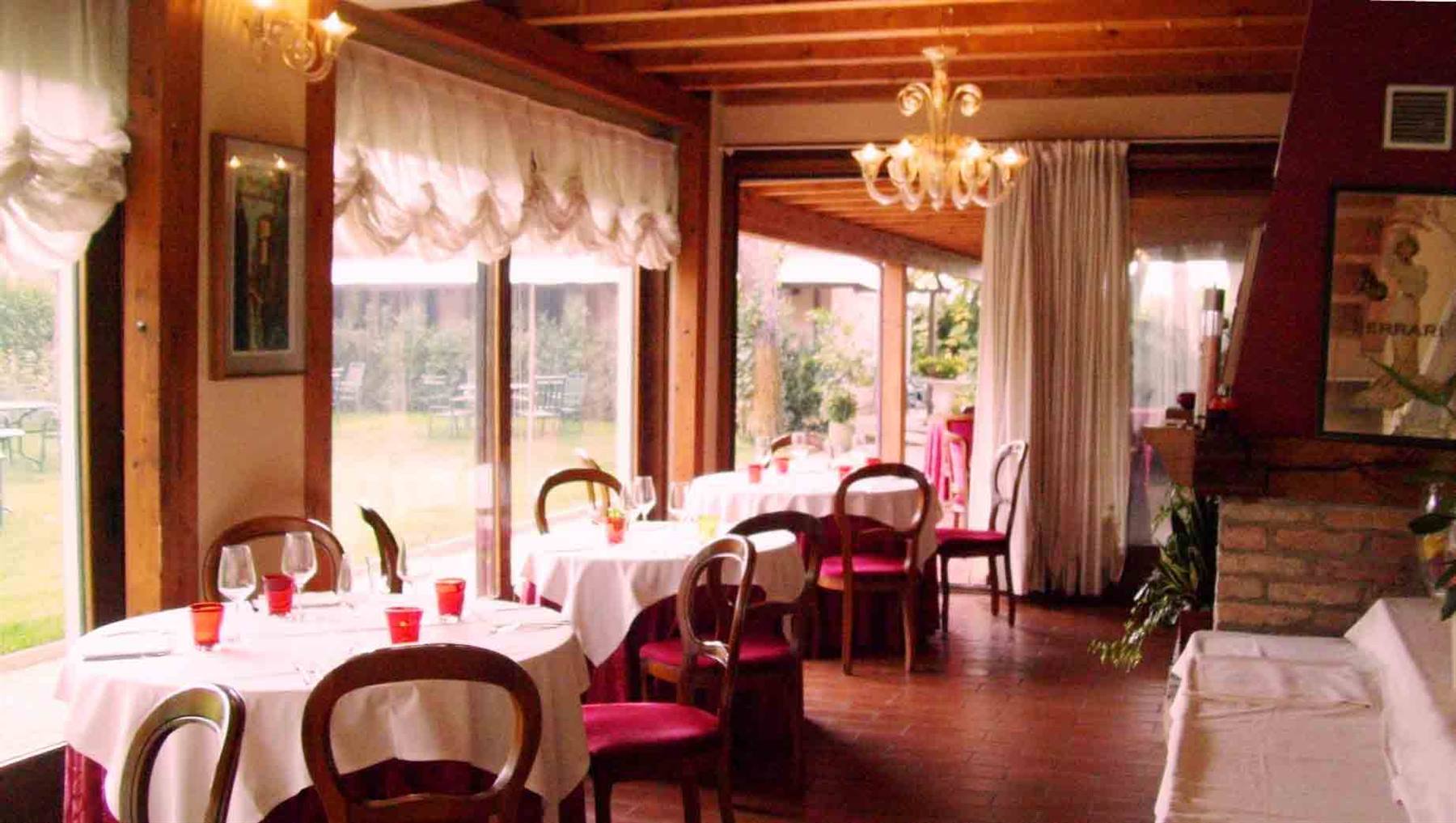 Sala di trattoria con tavoli apparecchiati, lampadario di vetro Murano e finestre sul giardino