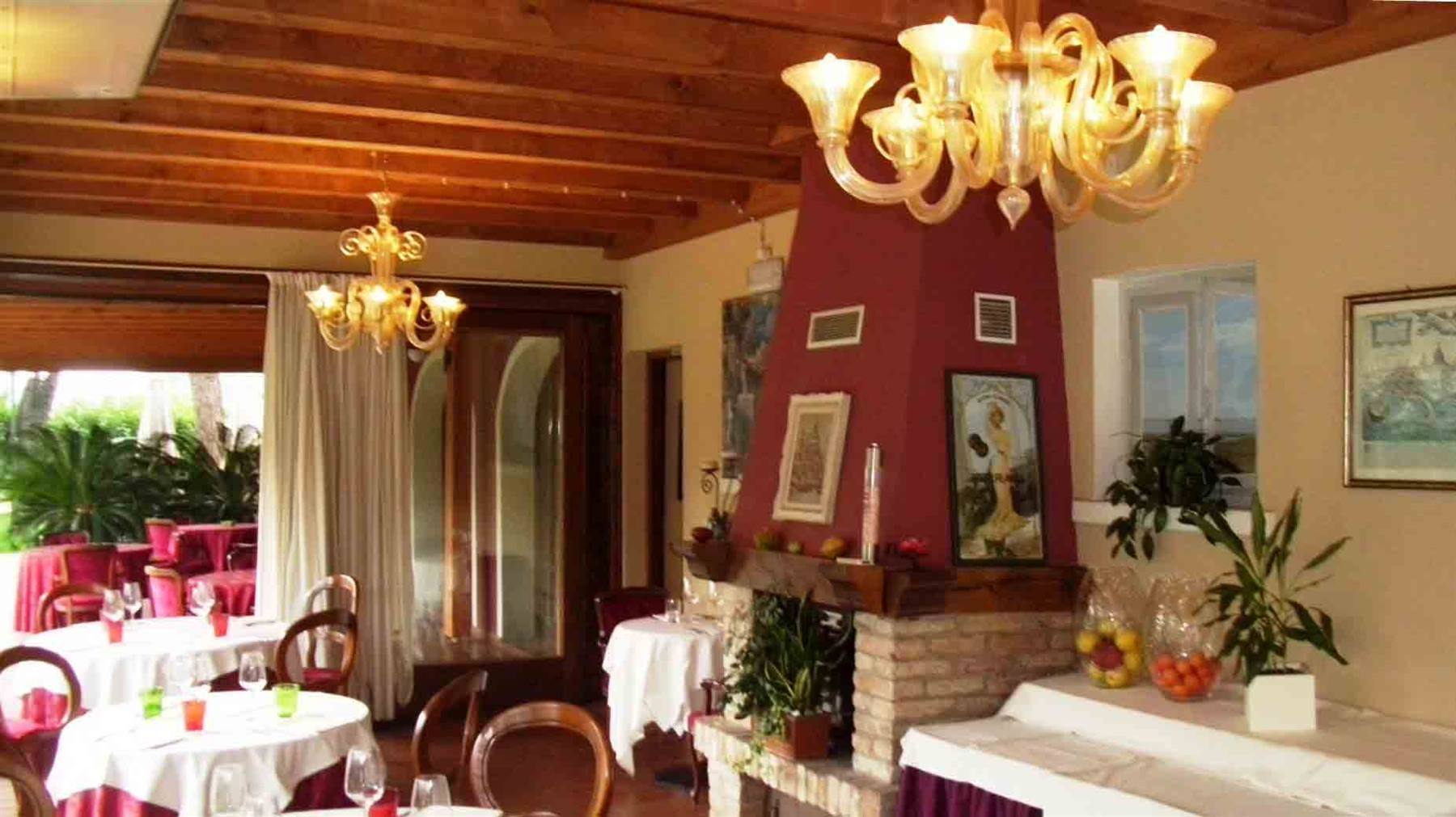 Sala di ristorante con lampadari in vetro di Murano, camino in mattoni e tavoli apparecchiati