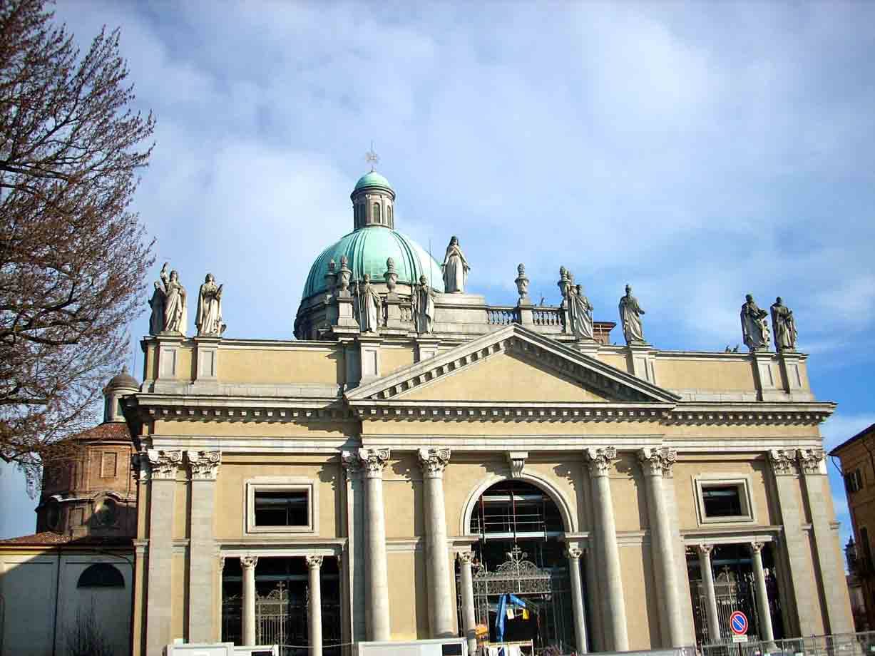 Facciata in pietra di una cattedrale con cupola verde e statue sotto cielo nuvoloso