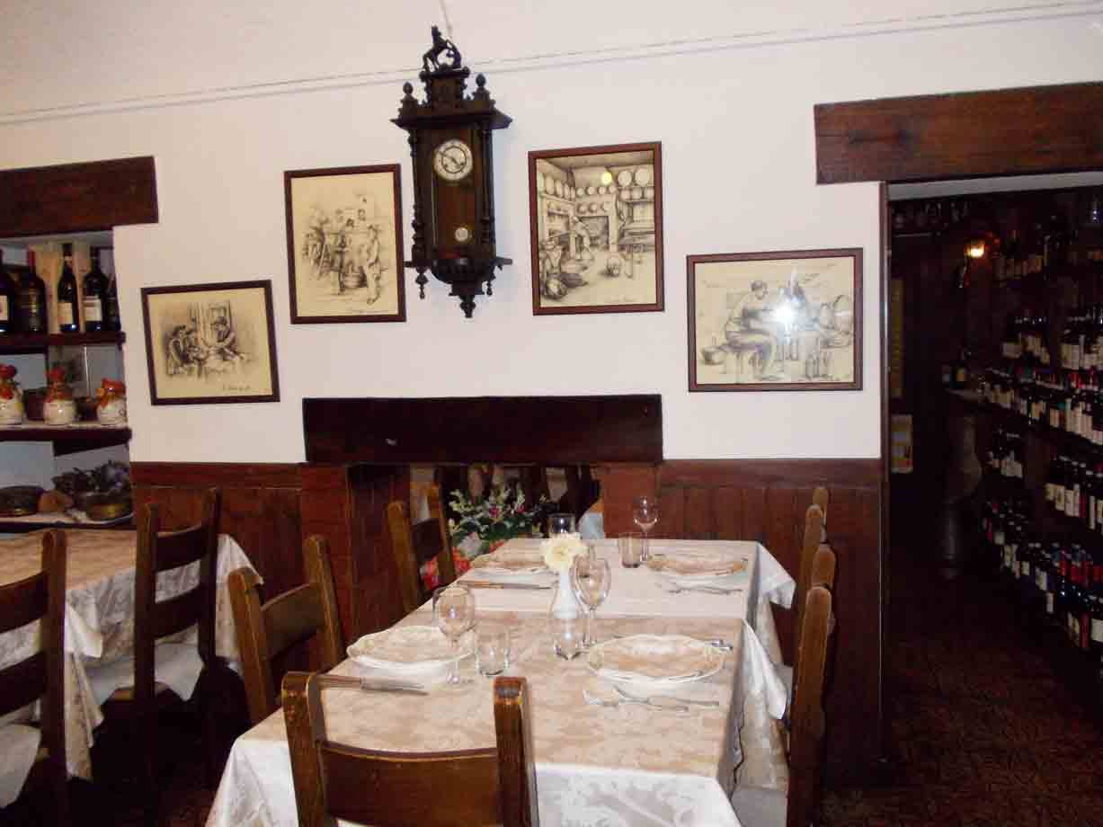 Sala di trattoria con tavolo apparecchiato, orologio a pendolo e stampe alle pareti