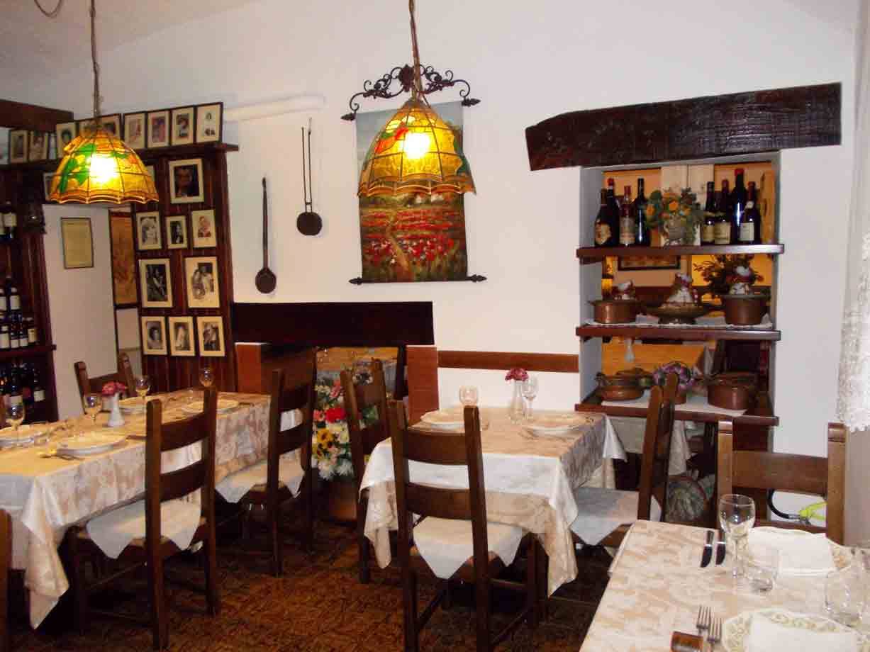 Sala di trattoria con tavoli apparecchiati, lampade Tiffany accese e bottiglie di vino