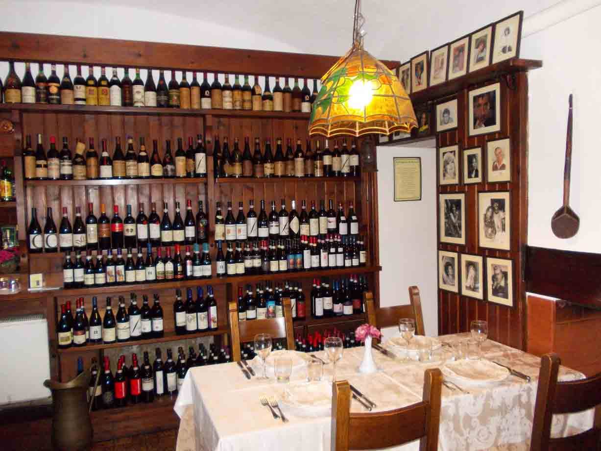 Sala di trattoria con scaffali di bottiglie di vino, tavola apparecchiata e lampada Tiffany