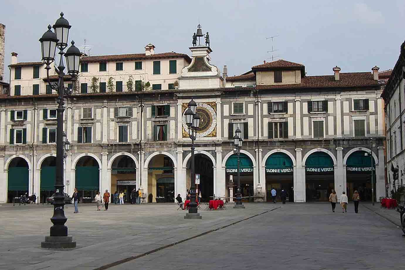 Turisti camminano in Piazza della Loggia a Brescia sotto la Torre dell'Orologio