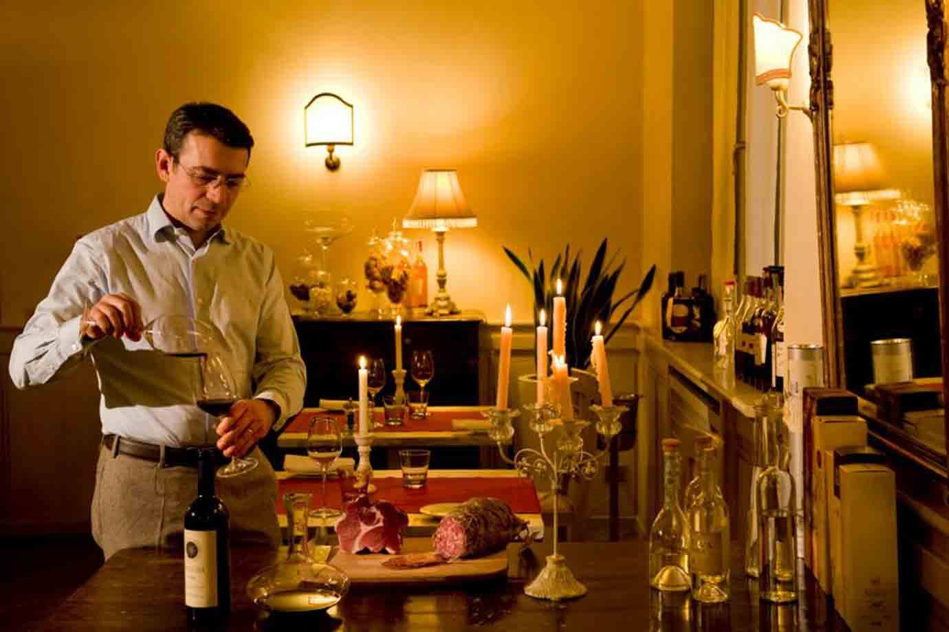 Cameriere versa vino accanto a salumi, candele accese e lampade illuminate