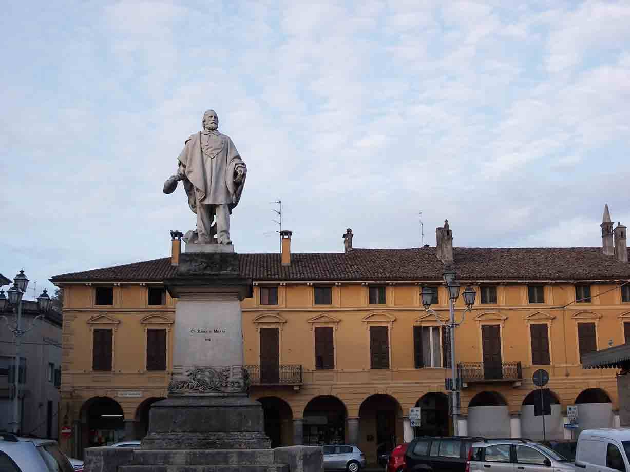 Statua in marmo su piedistallo davanti a palazzo giallo con portici