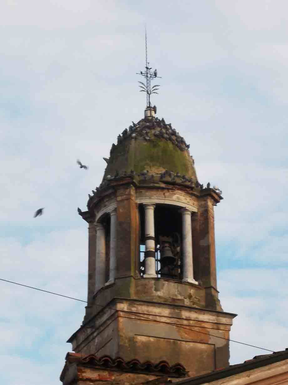 Campanile in mattoni con cupola verde e colombe, contro un cielo nuvoloso