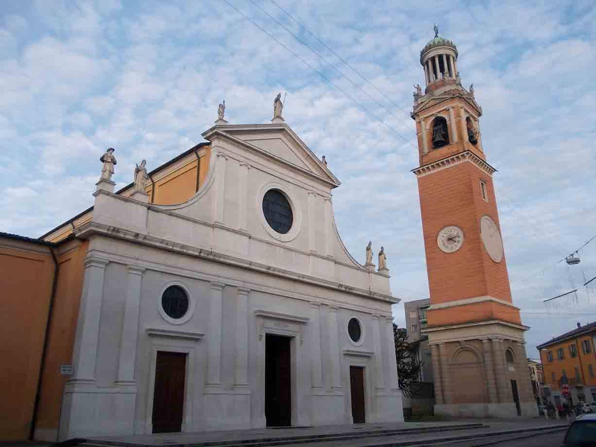 Facciata bianca di chiesa con statue e campanile in cotto sotto cielo nuvoloso