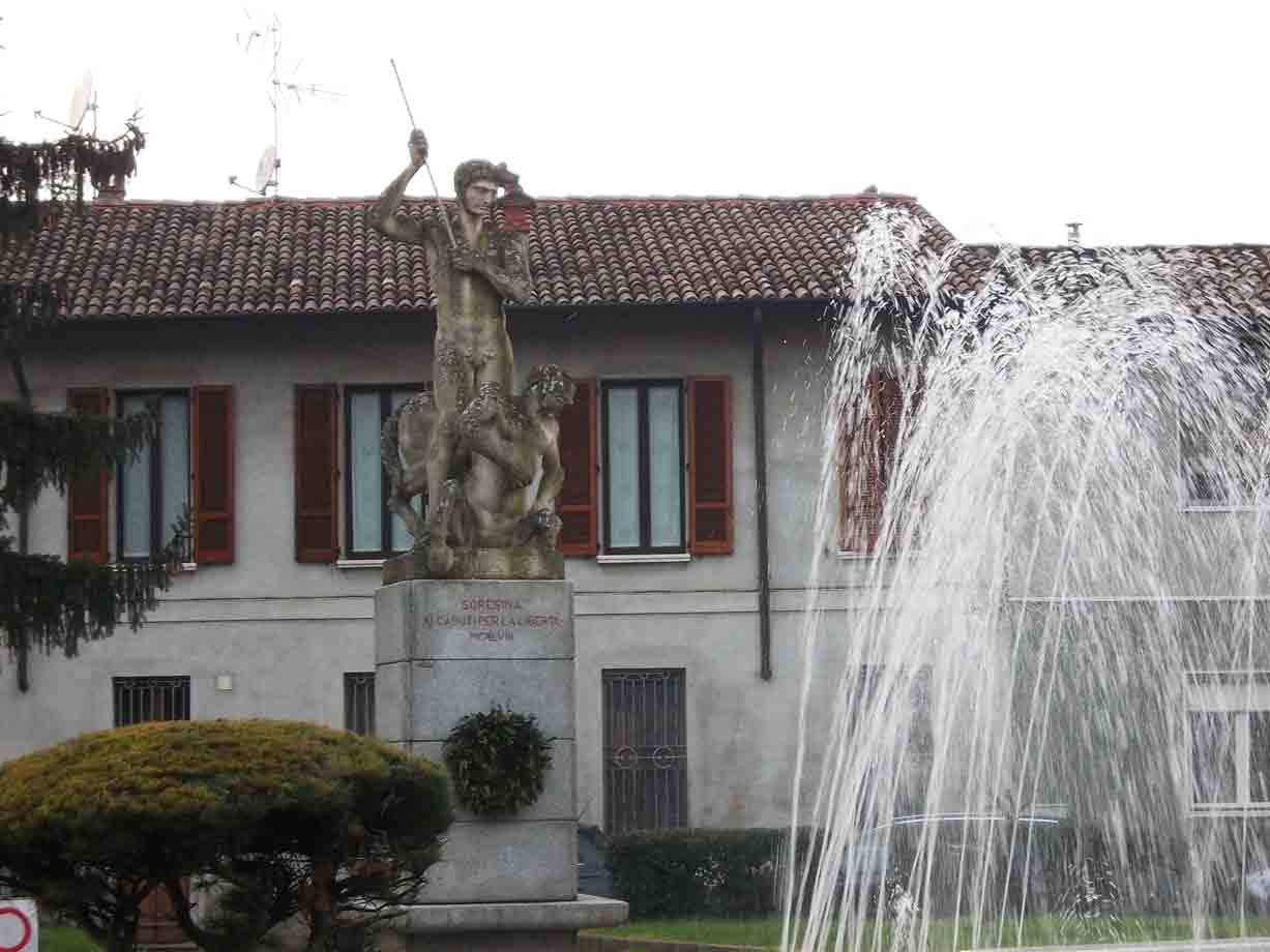 Statua in pietra su piedistallo davanti a edificio con tetti in coppi, getti d'acqua