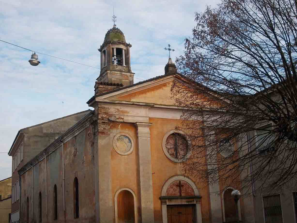 Chiesa intonacata ocra con campanile a cupola verde, rami spogli in primo piano