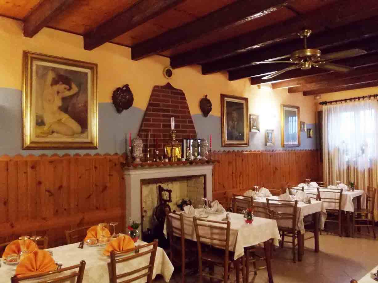 Sala di trattoria con tavoli apparecchiati, camino in mattoni e travi di legno