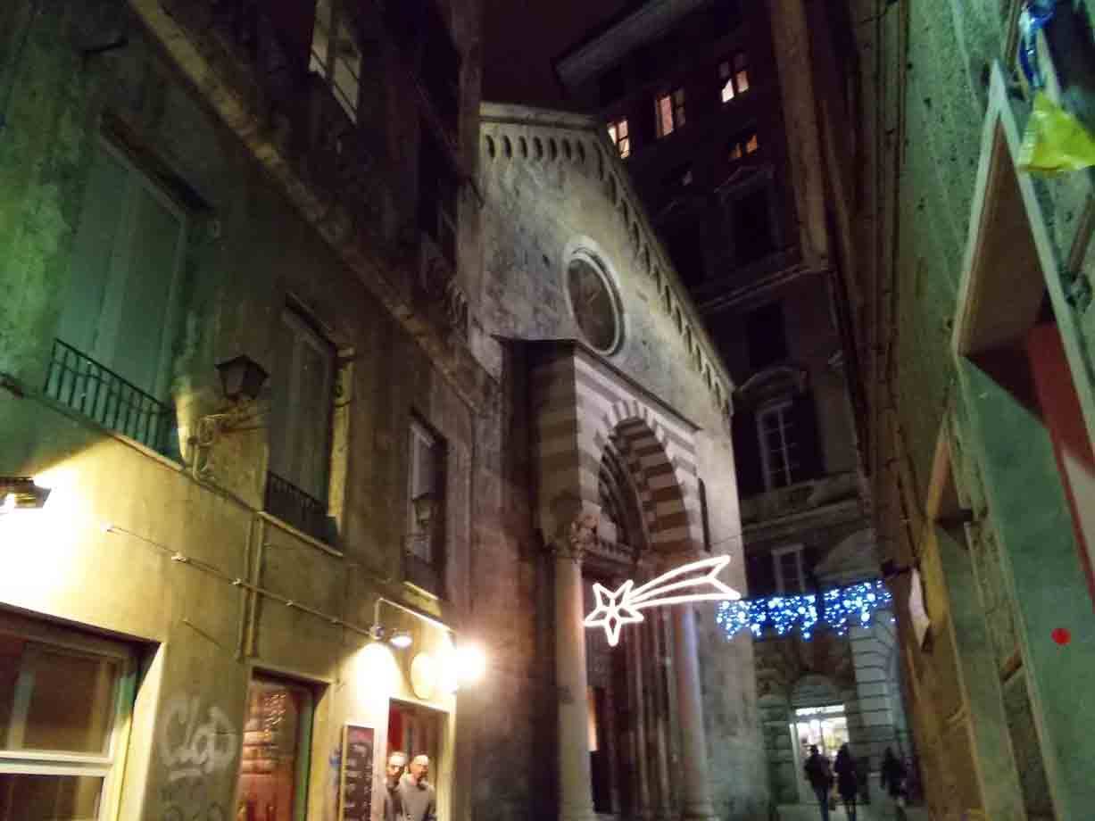 Vicolo notturno con facciata a fasce bianche e nere, luci natalizie a Genova