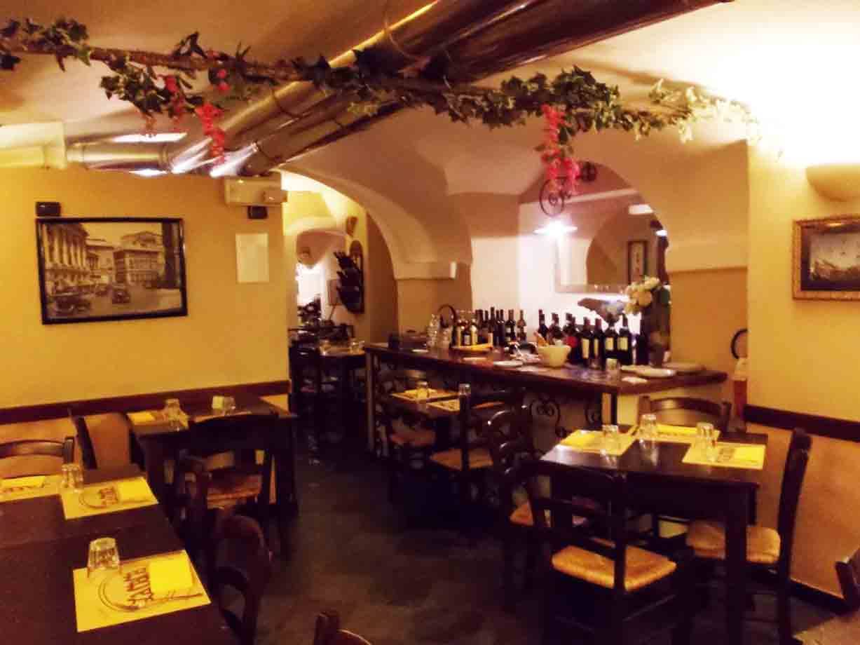 Sala di trattoria con volte, tavoli apparecchiati e bottiglie di vino al bancone