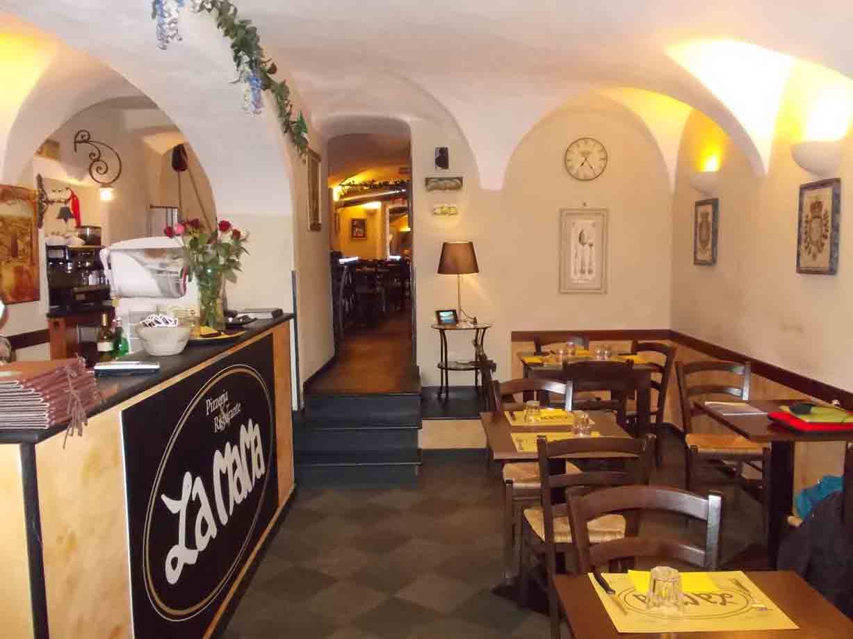 Sala di trattoria con volte bianche, bancone in legno, tavoli apparecchiati e luce calda