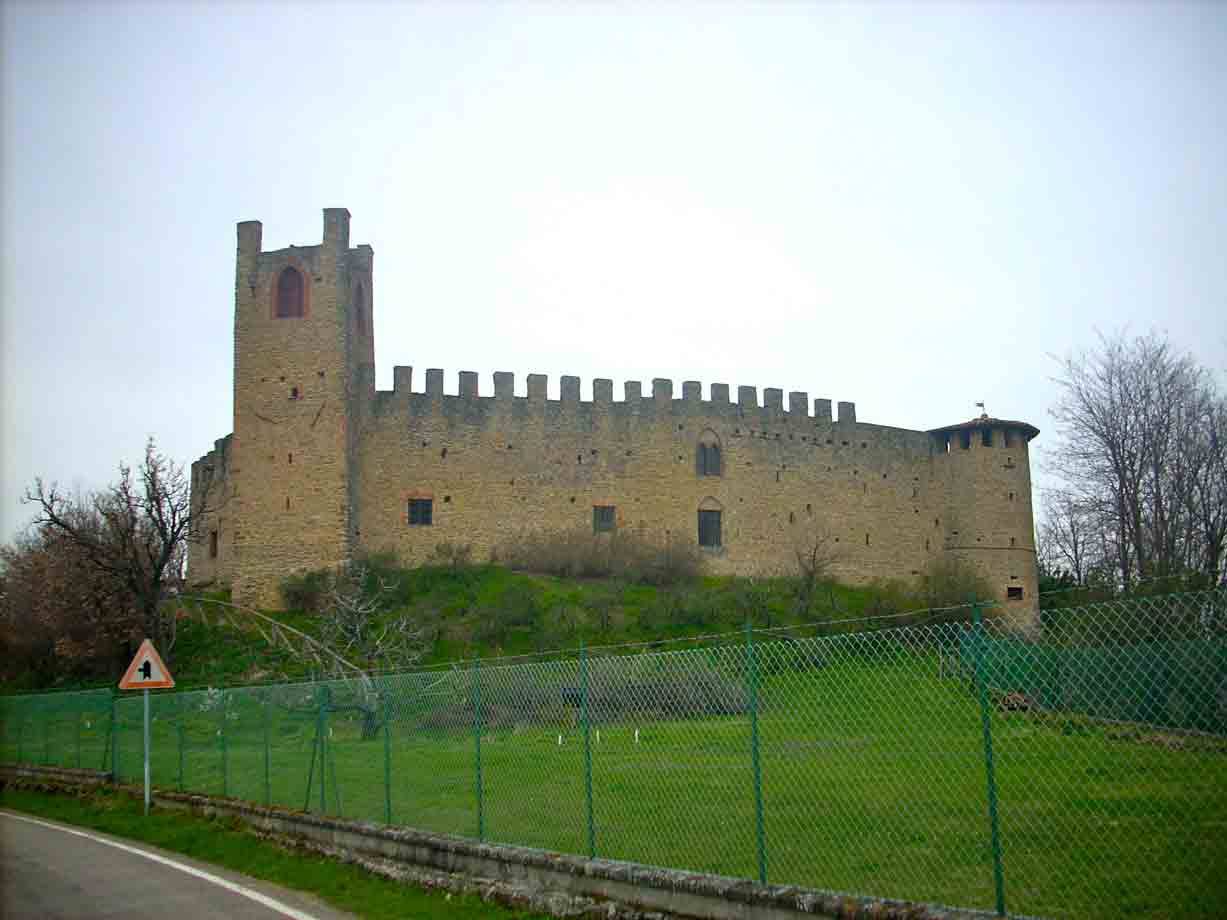 Rocca medievale in pietra con merlature e torre, recinzione verde e prato sotto