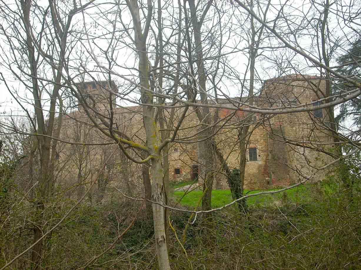 Castello medievale in pietra e mattoni dietro alberi spogli, luce grigia invernale