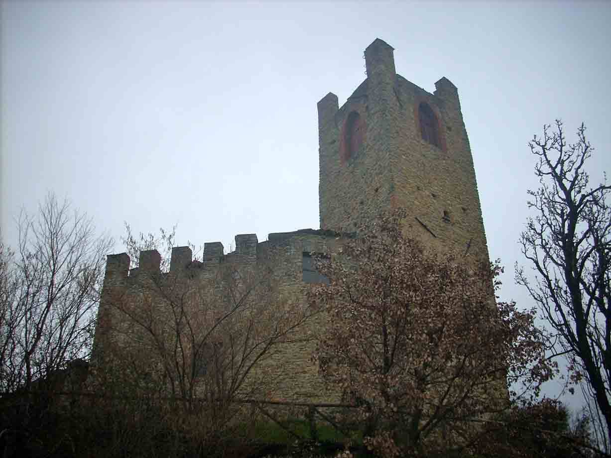 Castello medievale in pietra con torre merlata tra alberi spogli, cielo grigio