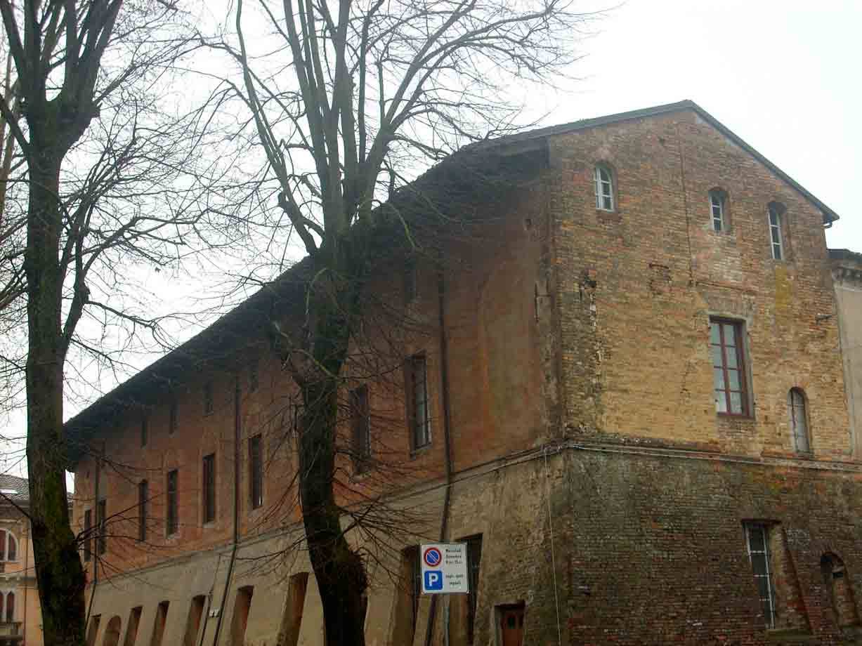 Antico edificio in mattoni ocra tra alberi spogli, cielo grigio invernale