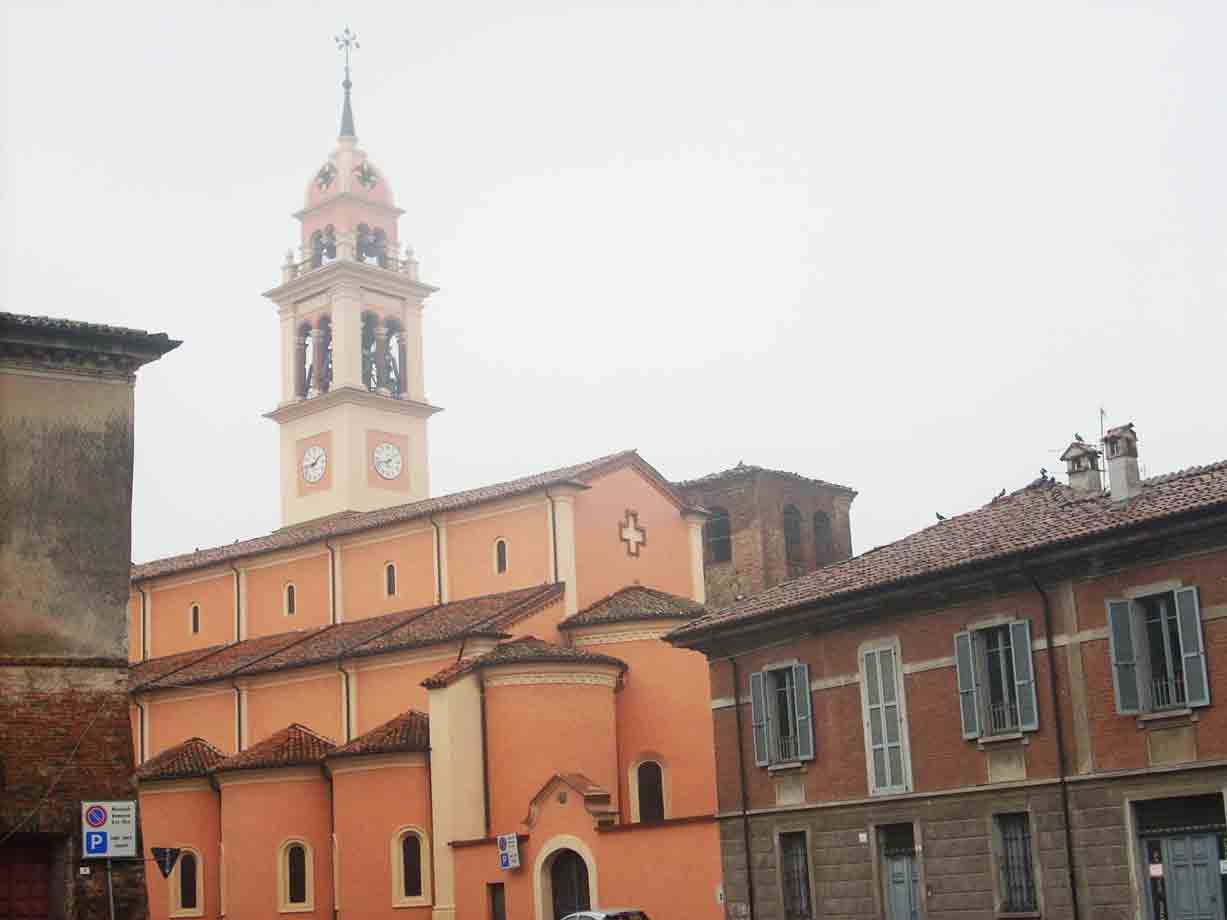 Chiesa color salmone con campanile e orologio tra case sotto cielo grigio