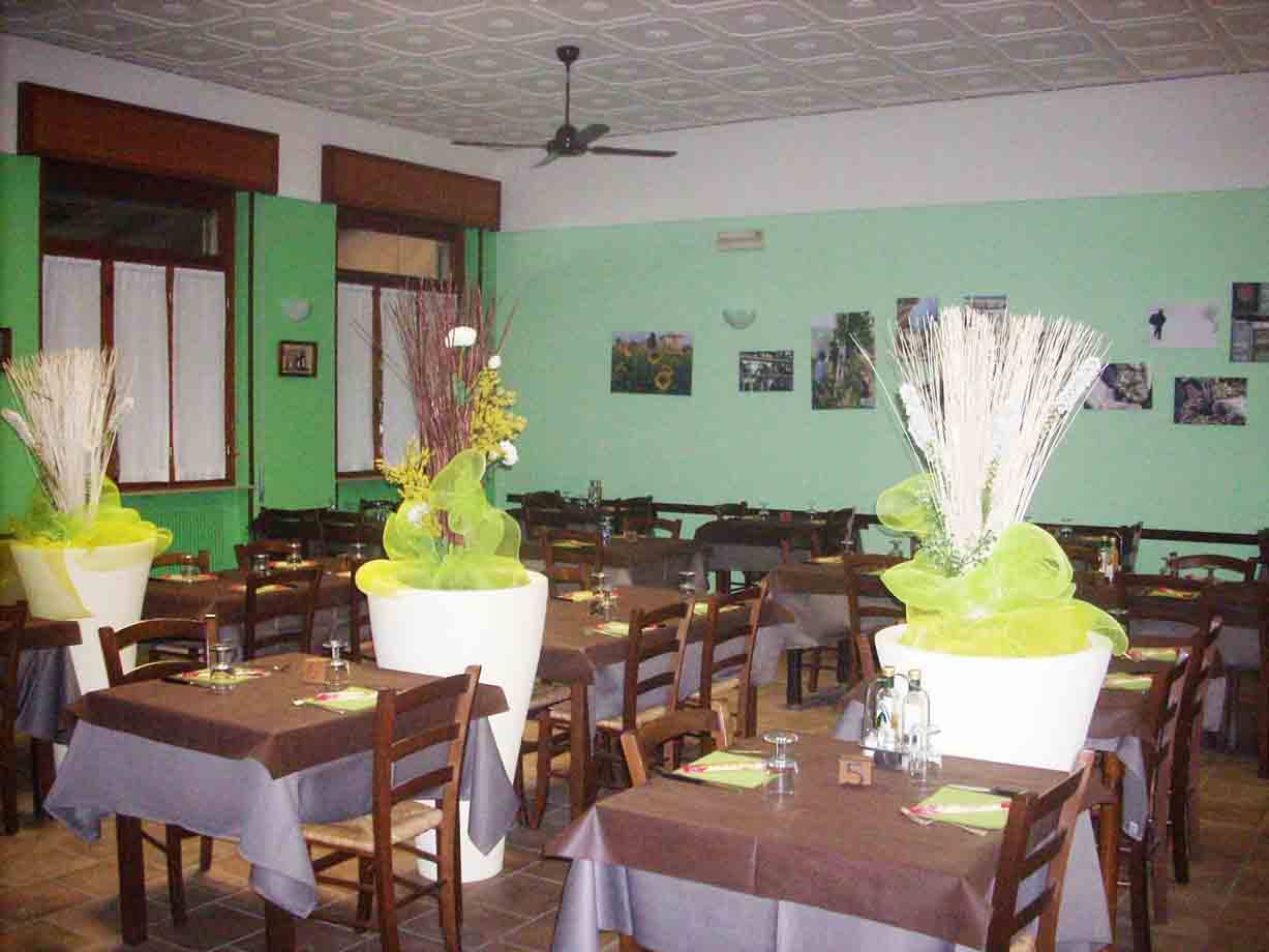 Sala ristorante con tavoli apparecchiati, pareti verdi e vasi bianchi decorati