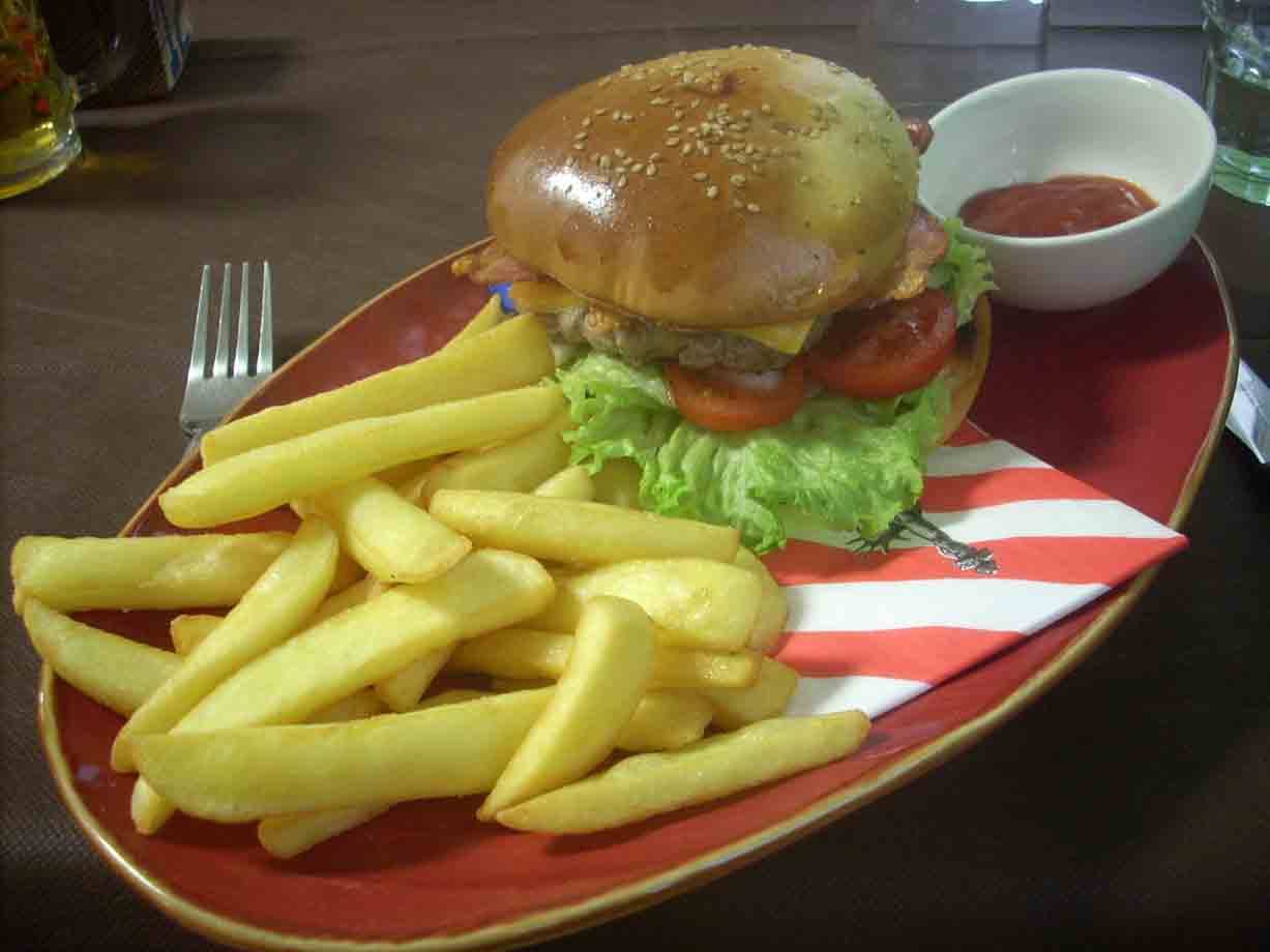 Hamburger con lattuga, pomodoro e patatine fritte su piatto rosso con ketchup