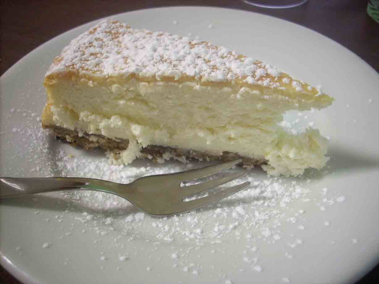 Fetta di cheesecake con zucchero a velo su piatto bianco, forchetta d'argento