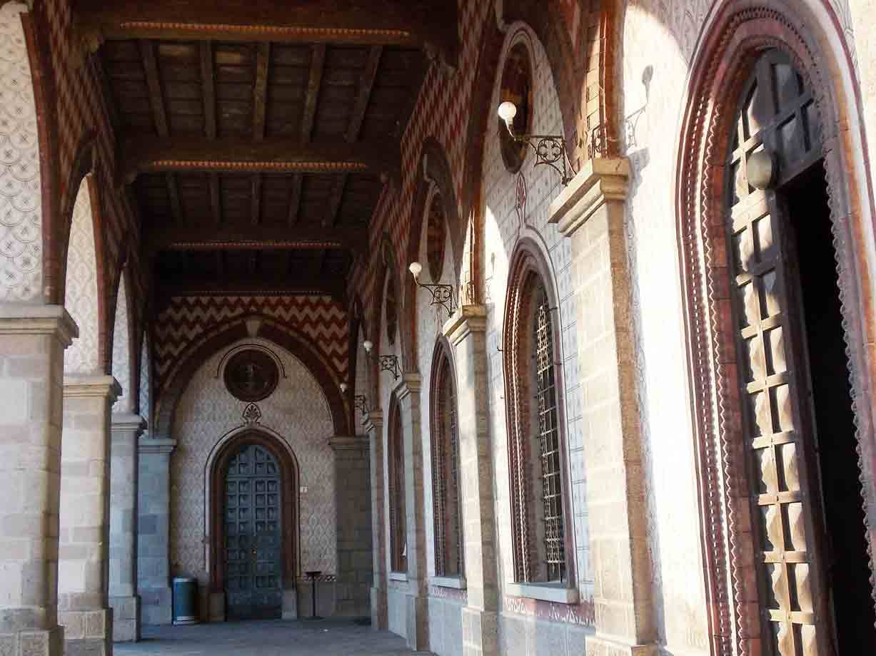 Portico con arcate in cotto e pietra, porte lignee, luce solare sulle colonne