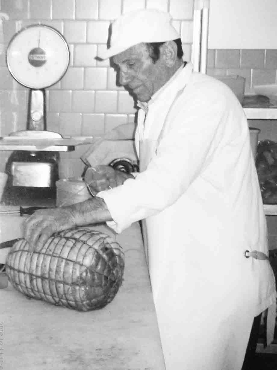 Macellaio in camice bianco prepara una porchetta legata in rete sul banco