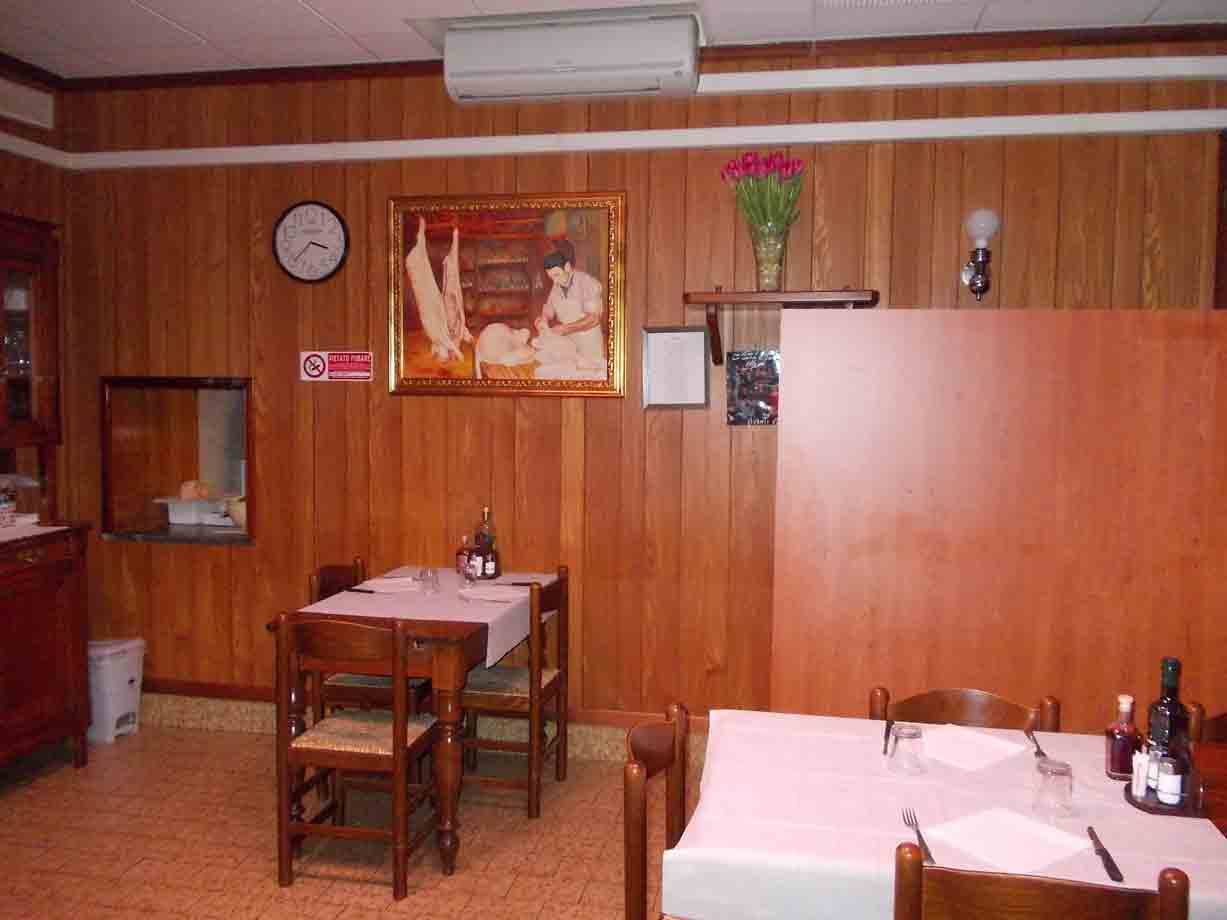 Sala di trattoria con pareti in legno, tavoli apparecchiati, quadro e fiori