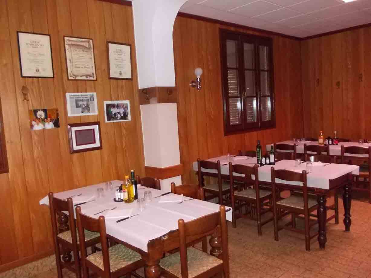 Sala di trattoria con pareti in legno, tavoli apparecchiati e certificati appesi