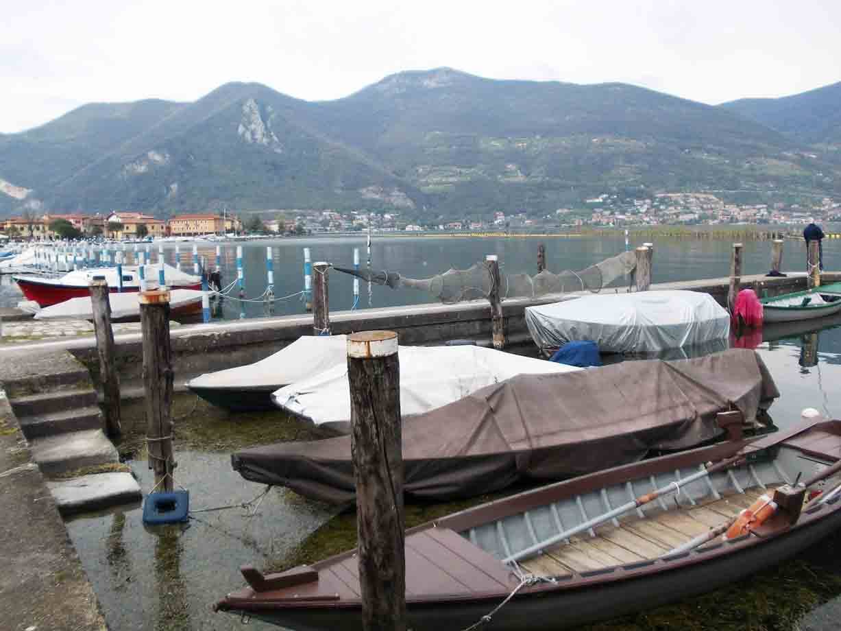 Barche di legno coperte ormeggiate al palo, lago Iseo con montagne