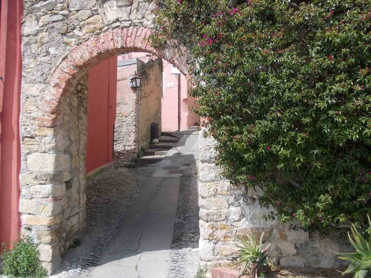 Arco di pietra con bouganville fiorita sopra un vicolo lastricato, muri rosa