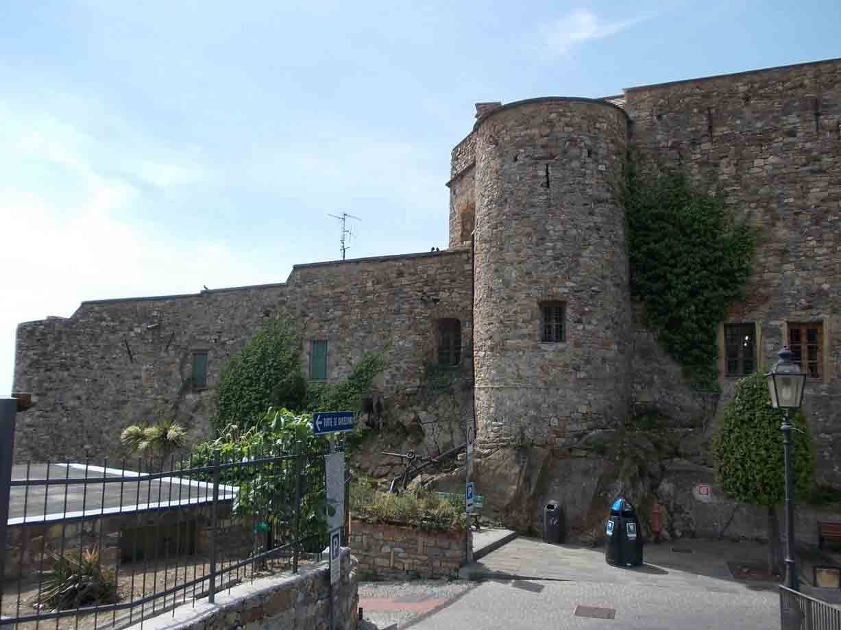 Torre cilindrica in pietra con edera, mura antiche e strada lastricata sotto