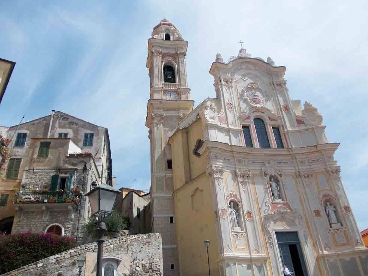 Chiesa barocca bianca con campanile accanto a case antiche, cielo azzurro