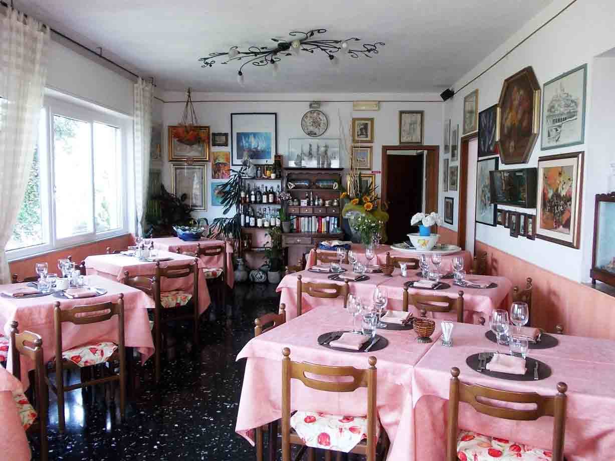 Sala di trattoria con tavoli apparecchiati, tovaglie rosa e quadri alle pareti
