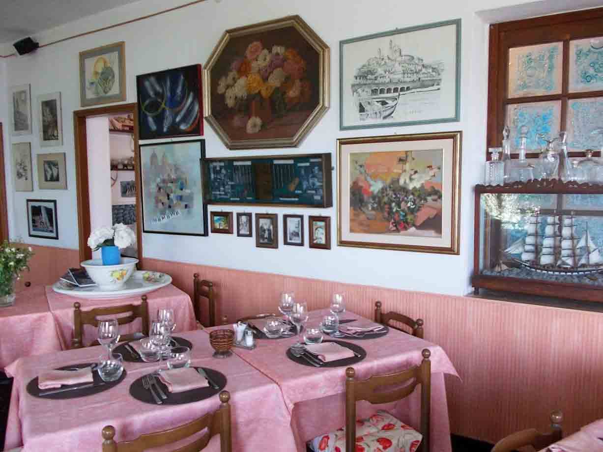 Sala di ristorante con tavoli apparecchiati, tovaglie rosa e quadri alle pareti