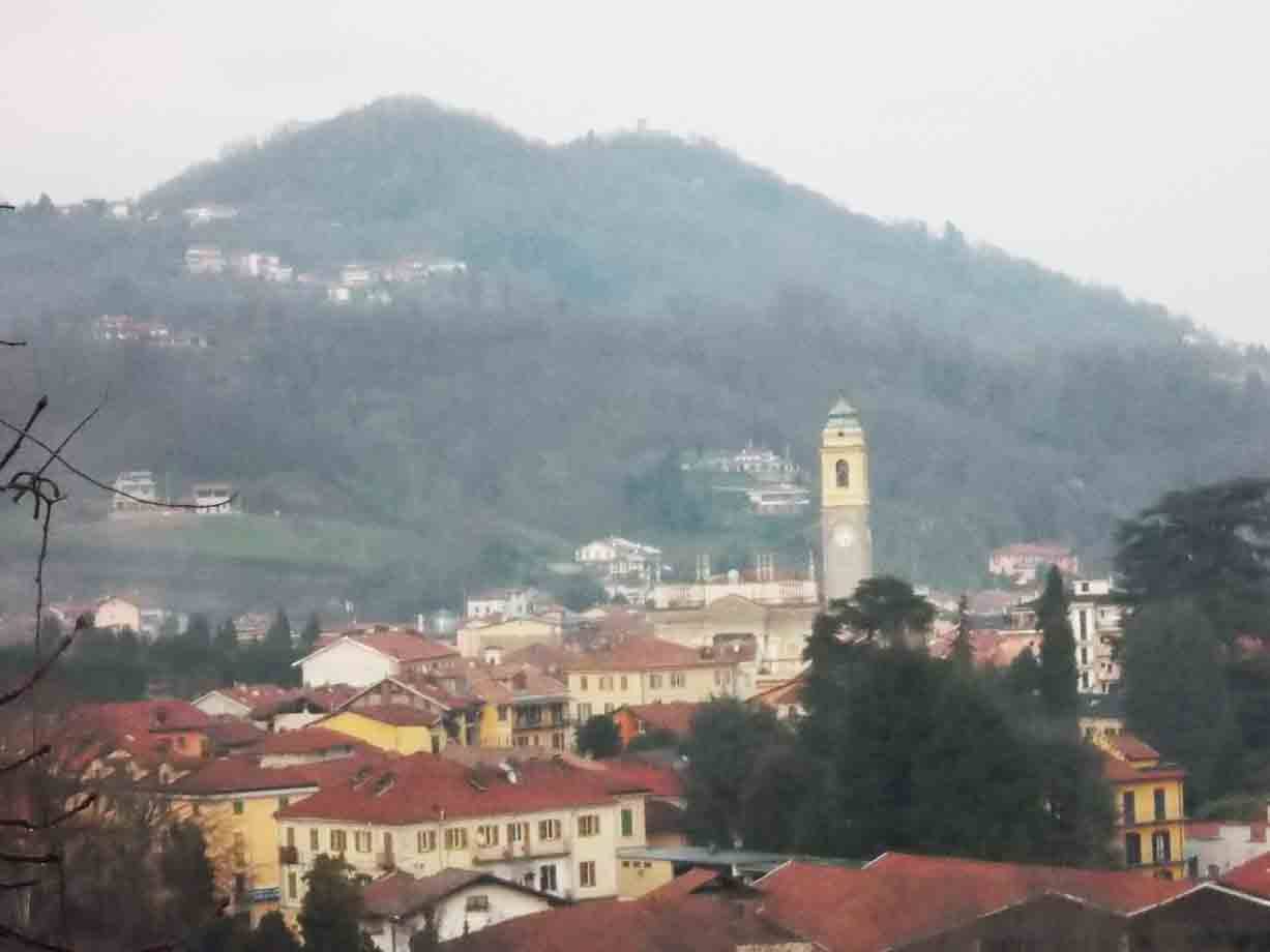 Campanile giallo sopra tetti rossi, collina nebbiosa sullo sfondo